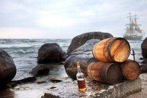 Bottle of rum by some barrels by a sea